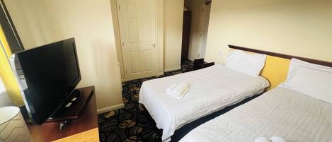 A hotel room with two beds, a TV, and a desk with a lamp.