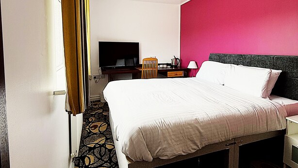 A hotel room with a bed, a desk, a chair, a television, and a patterned carpet. - Simplystay Lincoln Road (Skegness)