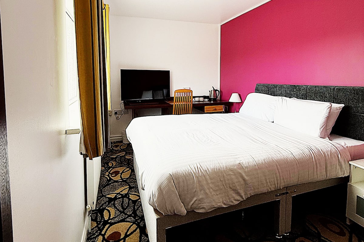 Habitación de hotel con cama, escritorio, silla, televisor y alfombra estampada.