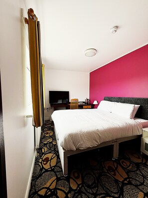 Een hotelkamer met een bed, een bureau, een stoel, een televisie en een kamerbreed tapijt met dessin.