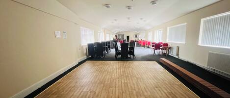 A spacious hall with a wooden floor, rows of tables and chairs, and a central aisle.