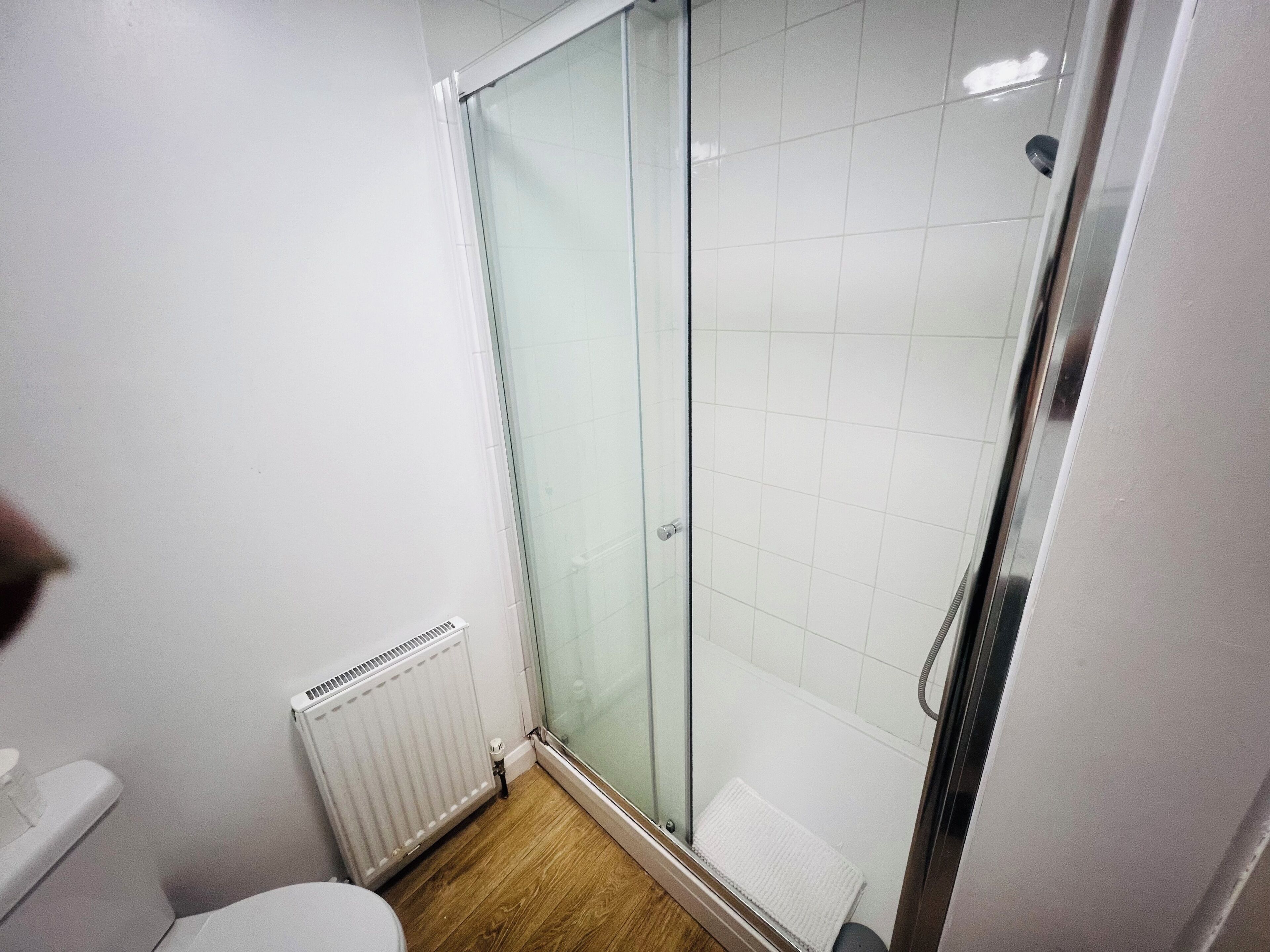 A bathroom with a glass shower enclosure, a white radiator, and a wooden floor.