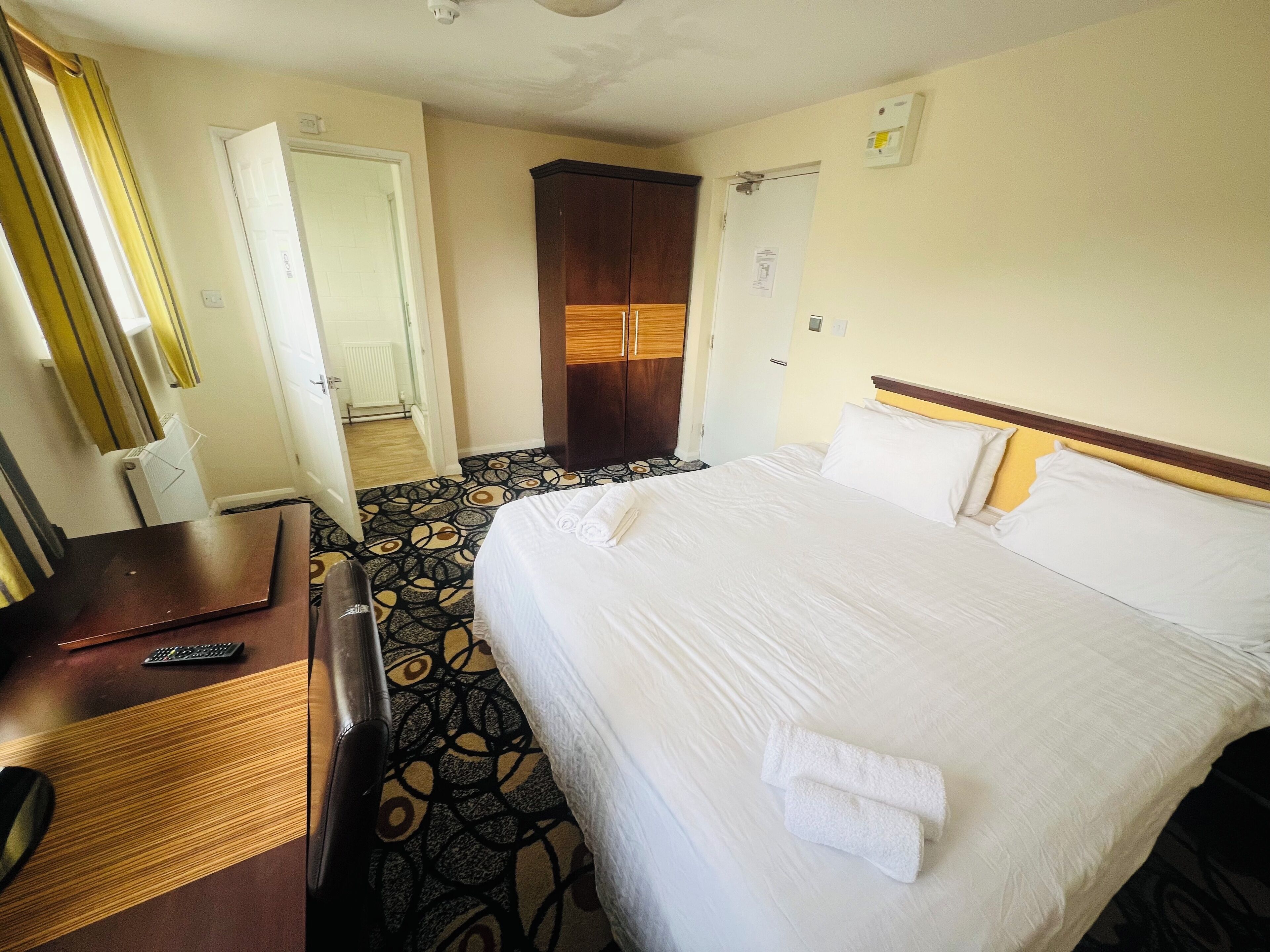 A hotel room with a bed, a desk, a chair, a wardrobe, and a bathroom door.