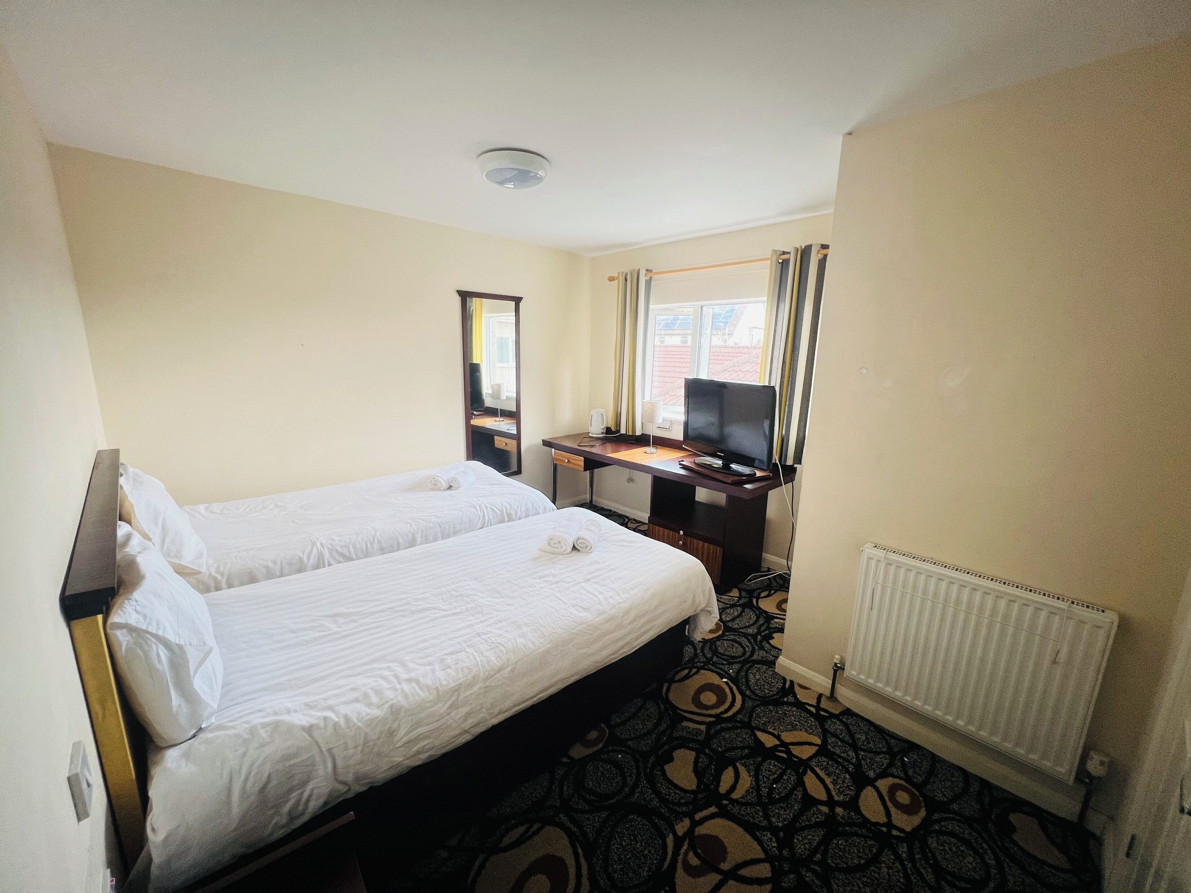 Een hotelkamer met twee eenpersoonsbedden, een bureau met een computer, een televisie en een raam met gordijnen.