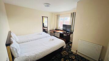 A hotel room with two single beds, a desk with a computer, a TV, and a window with curtains.