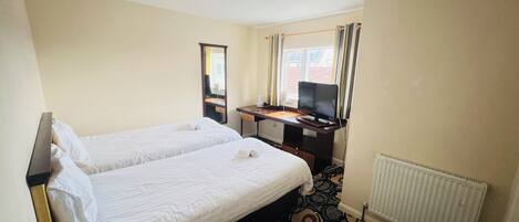 Une chambre d’hôtel avec deux lits simples, un bureau avec un ordinateur, une télévision et une fenêtre avec des rideaux.