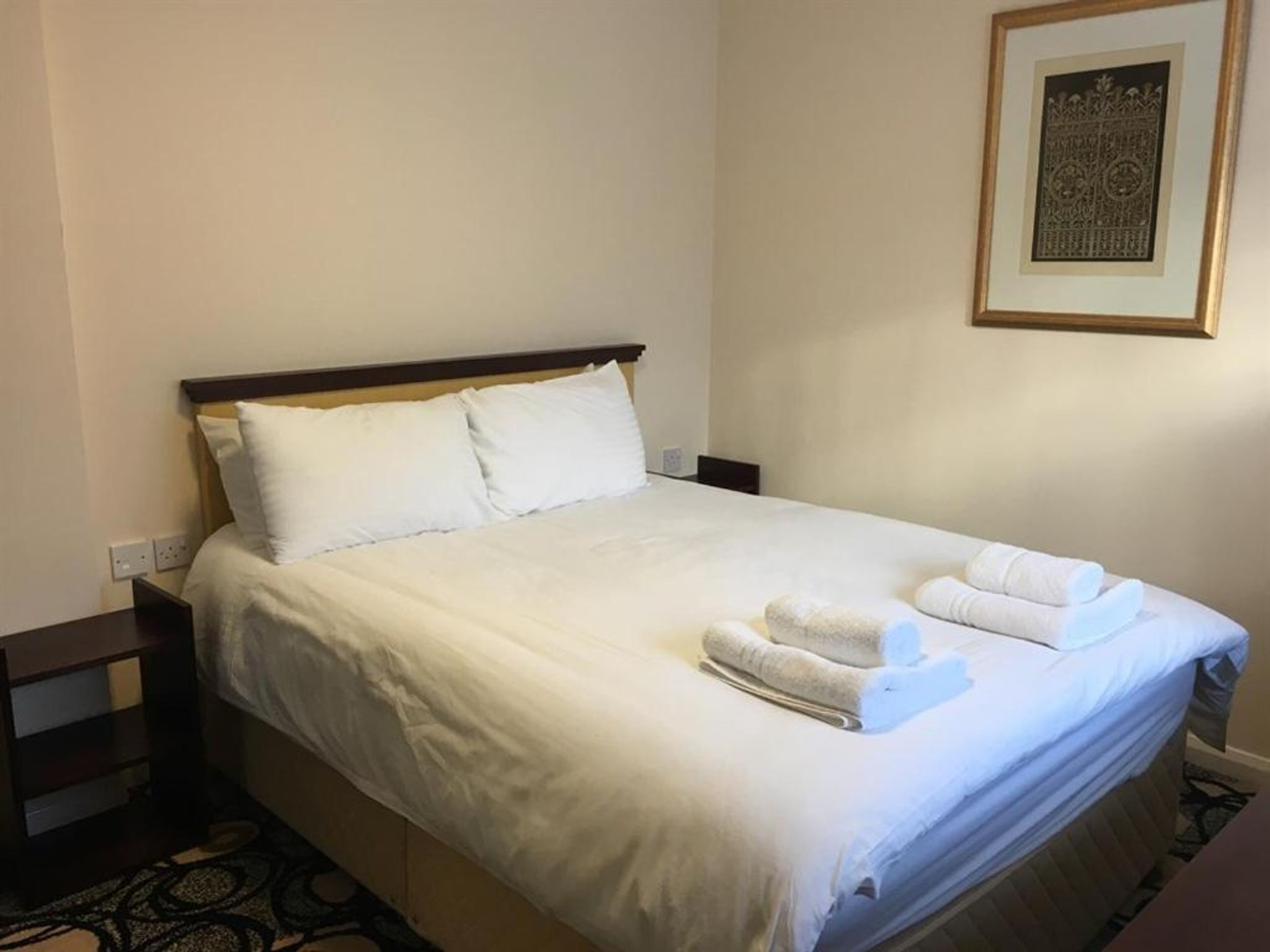 Una cama bien hecha con sábanas blancas y dos toallas dobladas en el reposapiés.