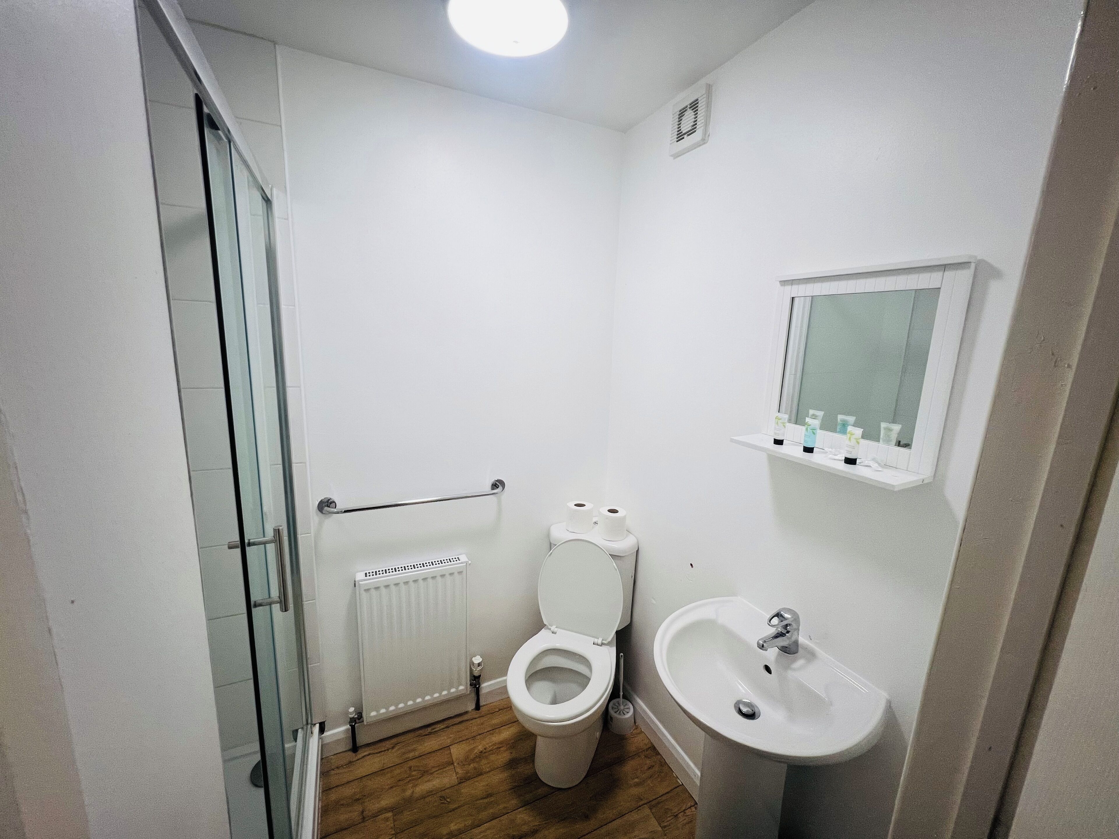 A small, modern bathroom with a toilet, sink, and glass shower enclosure.