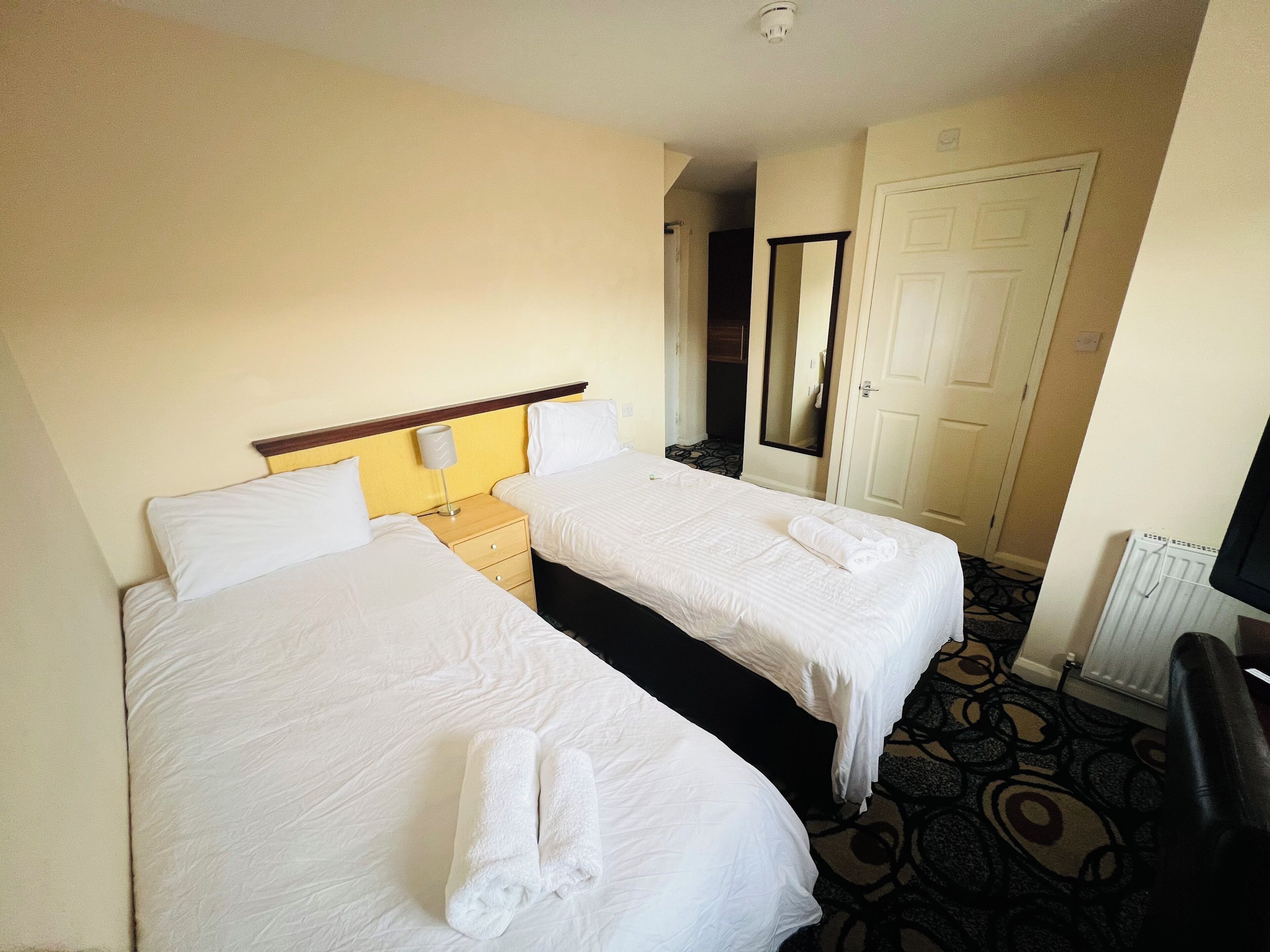 A hotel room with two beds, a nightstand, a mirror, and a radiator.