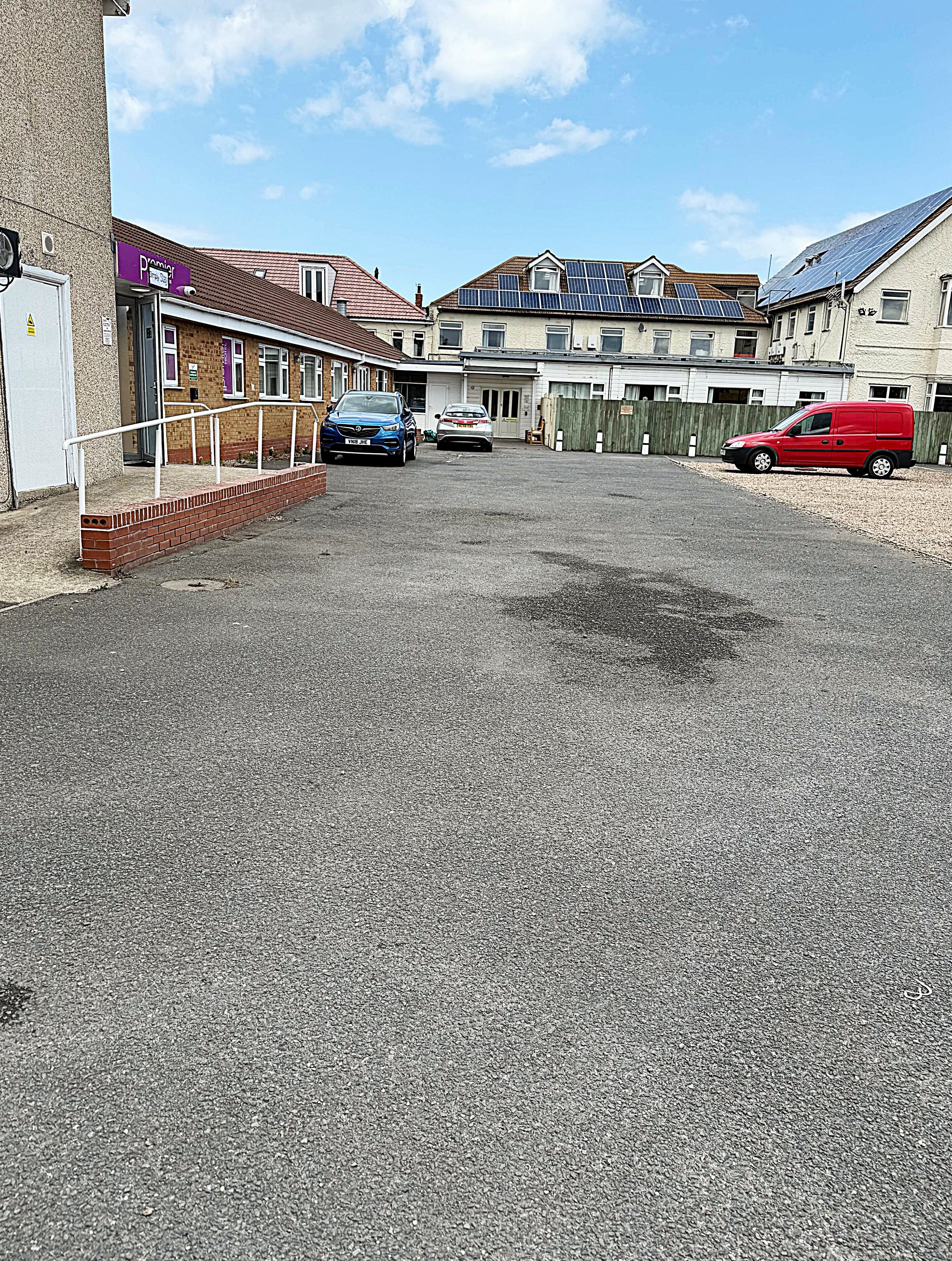 A residential street with houses, a gravel driveway, and parked cars.