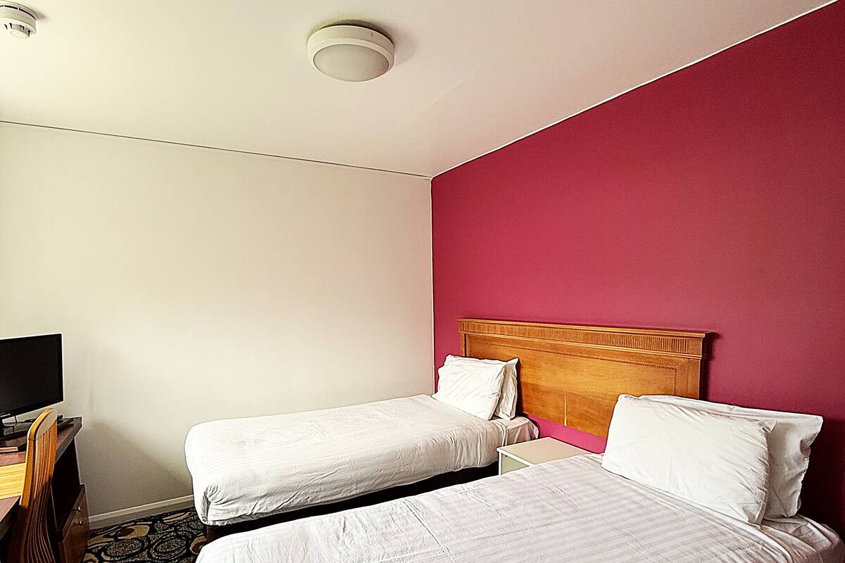 Habitación de hotel con dos camas individuales, cabecero de madera, un escritorio con silla y televisor.