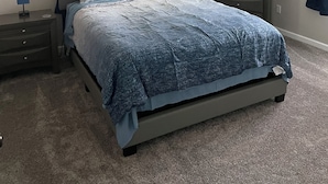 Ein Schlafzimmer mit einem Bett, einem Nachttisch, einer Kommode, einem Deckenventilator und einem Fenster mit Vorhängen.