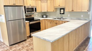 Una cocina con armarios de madera, un refrigerador de acero inoxidable, un microondas, un horno y un lavabo.