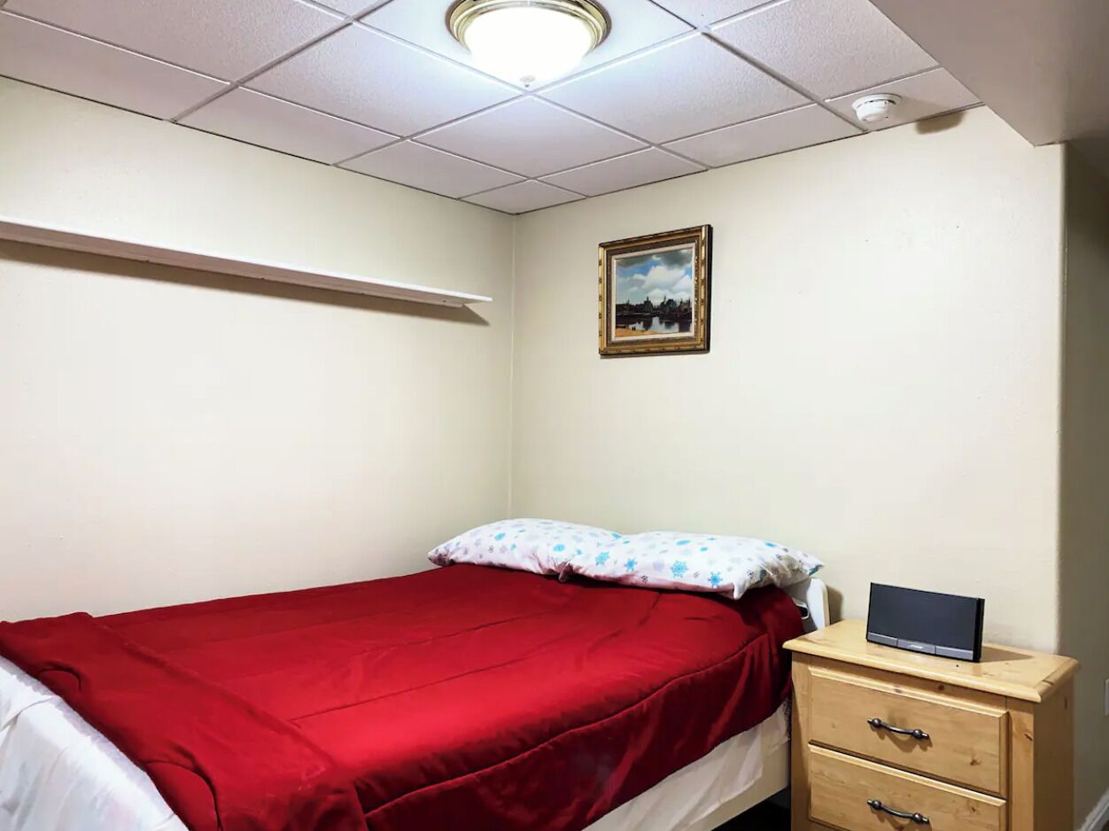 Ein kleines, ordentlich eingerichtetes Schlafzimmer mit einem Einzelbett, einem Nachttisch mit einem Laptop und einem gerahmten Bild an der Wand.