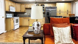A kitchen with wooden cabinets, a microwave, stove, and refrigerator. There is a table with a lamp and books. - Cozy Private Suite with Kitchen, Gym, and More in UT! (Draper)