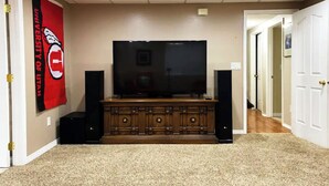 A home entertainment room with a TV on a wooden cabinet, two speakers, and a carpeted floor. - Cozy Private Suite with Kitchen, Gym, and More in UT! (Draper)