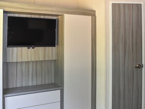 Ein Zimmer mit an der Wand befestigtem Fernseher, einer Tür mit strukturierter Verkleidung und einem weißen Schrank.