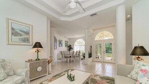 Un vaste salon doté d’un haut plafond, un coin repas avec des meubles blancs et une vue dégagée grâce à de grandes fenêtres.