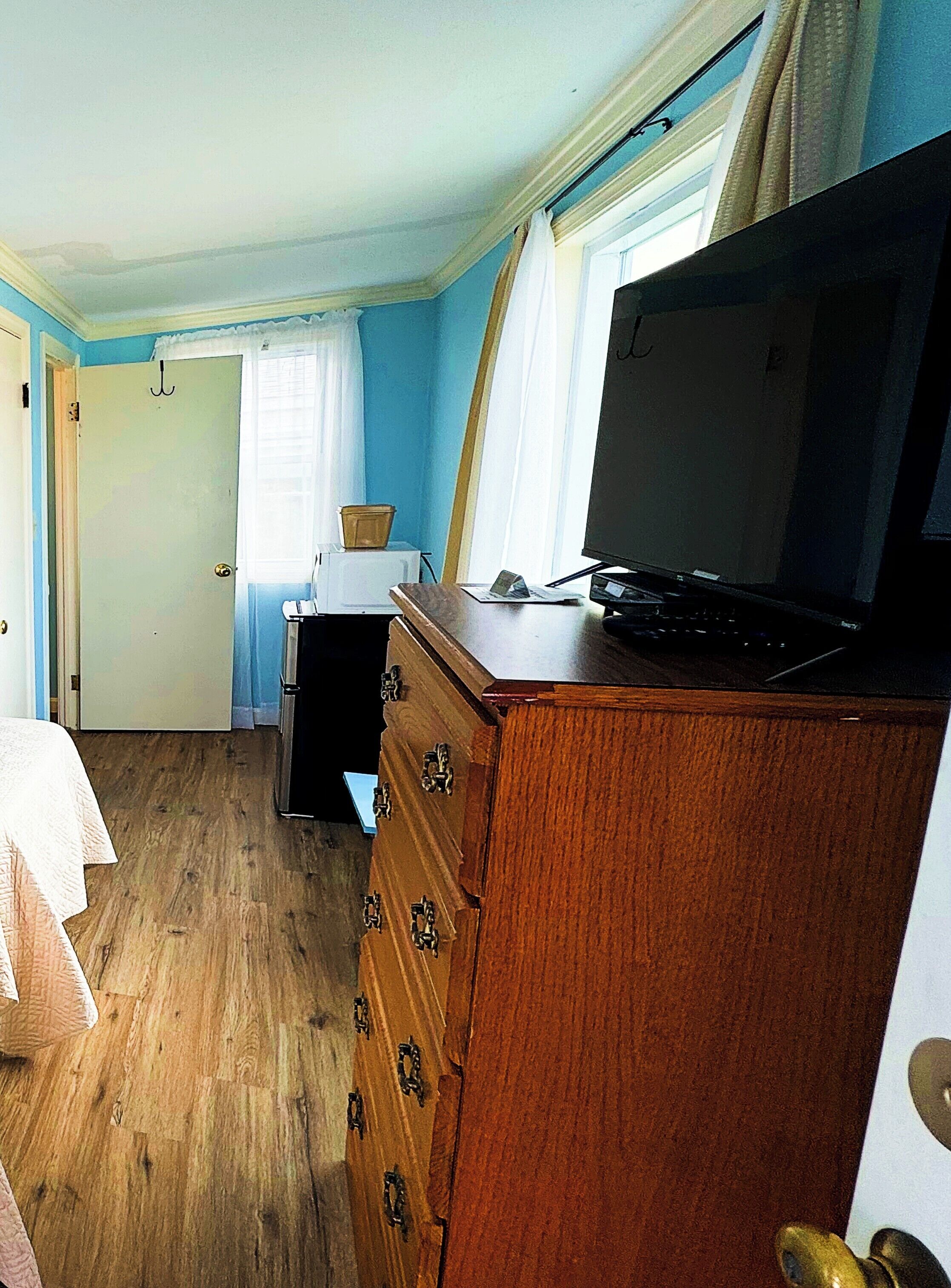A bedroom with a wooden dresser, a bed, a desk, and a television.