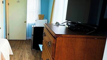 A bedroom with a wooden dresser, a bed, a desk, and a television.