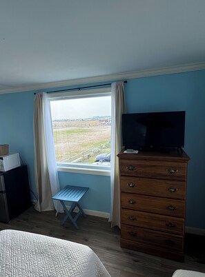 Ein Zimmer mit einem Bett, einem Holzschrank, einem Fernseher darauf, einem kleinen Tisch und einem Fenster mit Vorhängen.