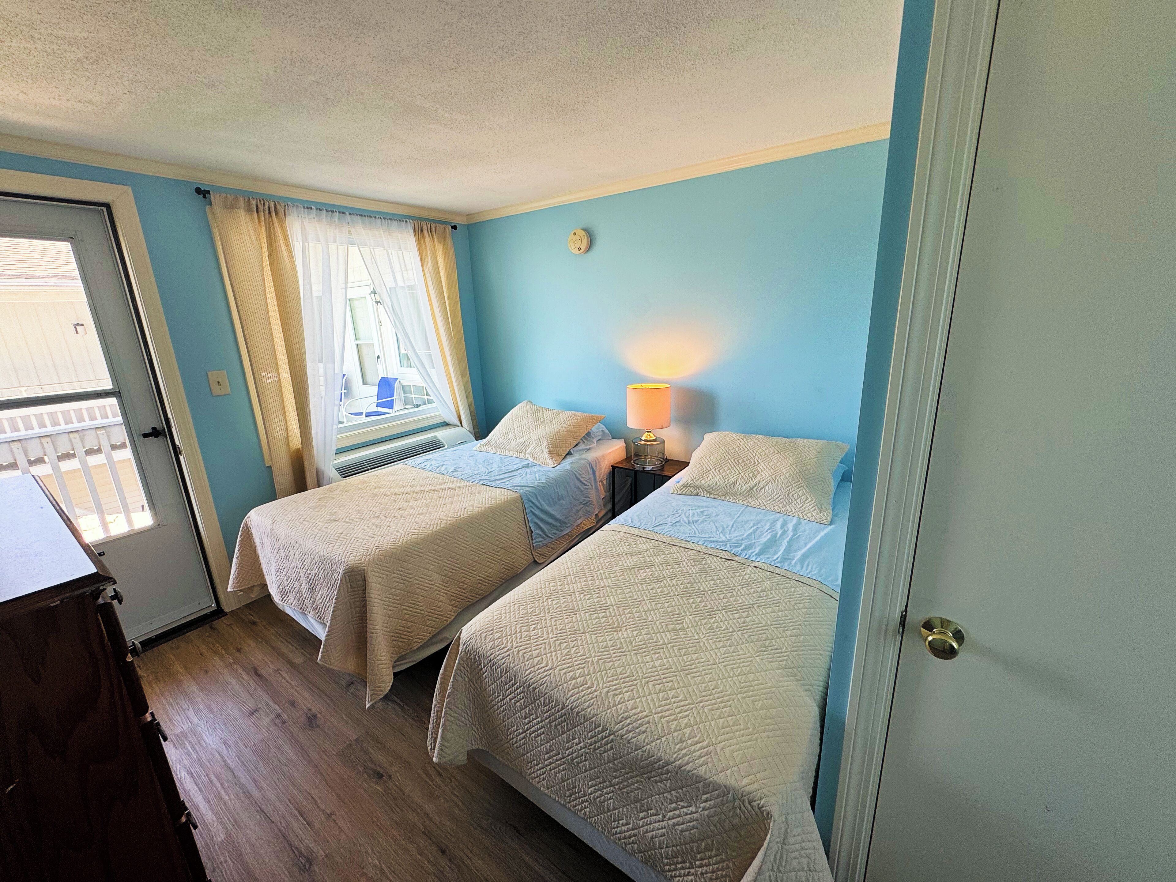 Une chambre avec deux lits, une fenêtre avec des rideaux, une lampe de chevet et une porte.