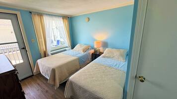 Une chambre avec deux lits, une fenêtre avec des rideaux, une lampe de chevet et une porte.