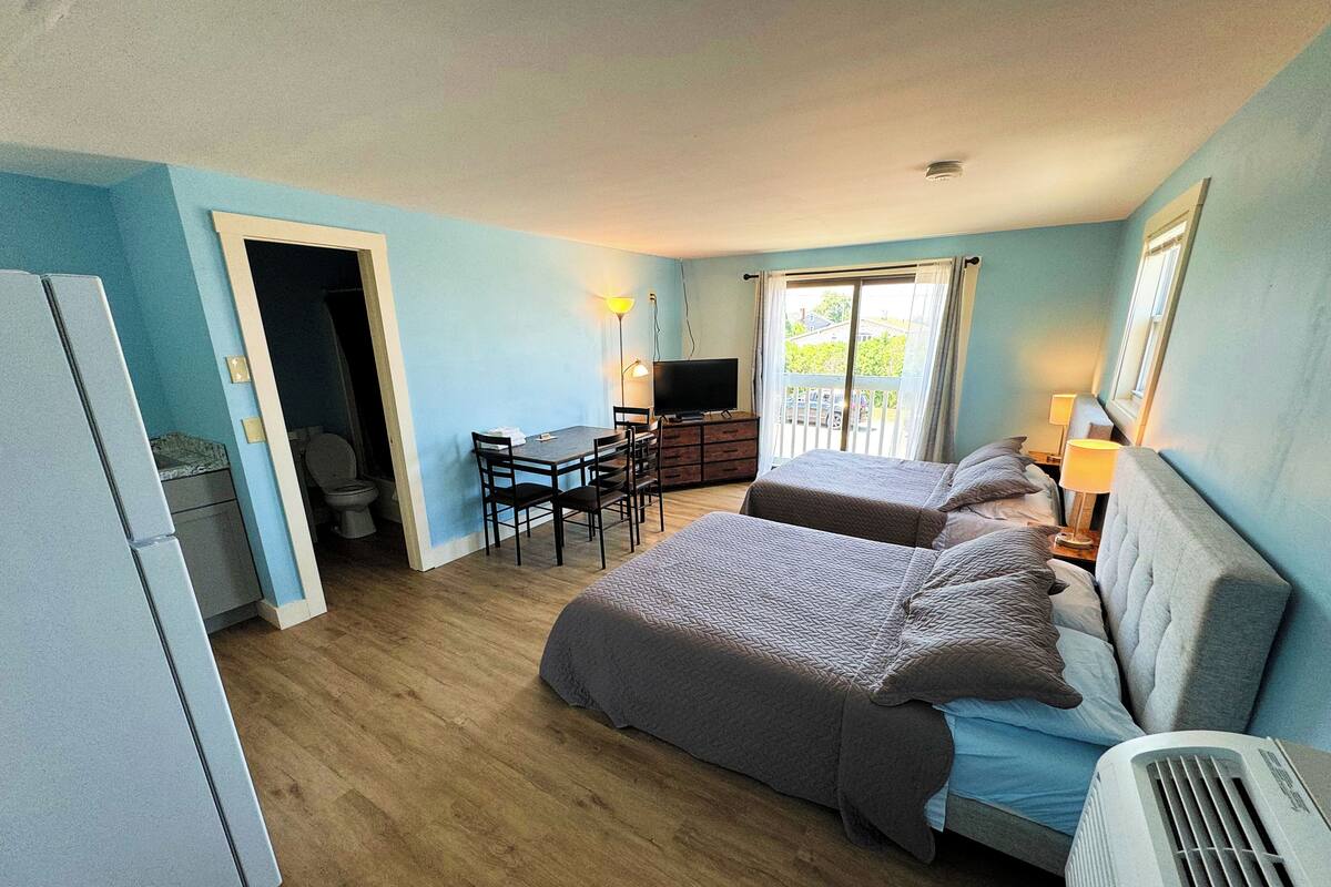 A hotel room with two beds, a desk, a television, and a balcony with curtains.