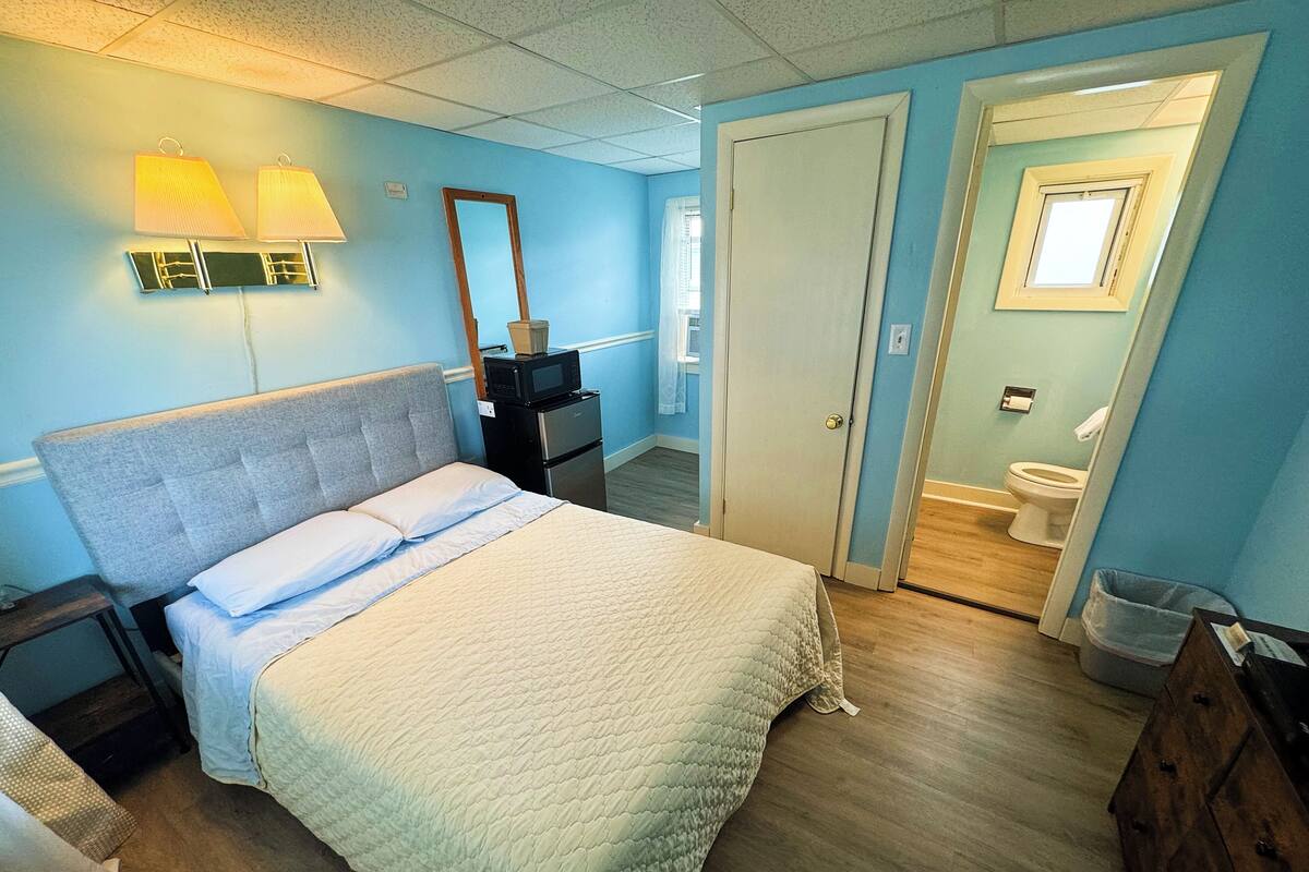 A bedroom with a bed, nightstand, dresser, and a bathroom visible through an open door.