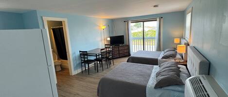 Quarto com duas camas, uma escrivaninha, televisão e varanda com vista.