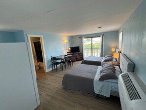 Ein Zimmer mit zwei Betten, einem Schreibtisch, einem Fernseher und einem Balkon mit Blick.