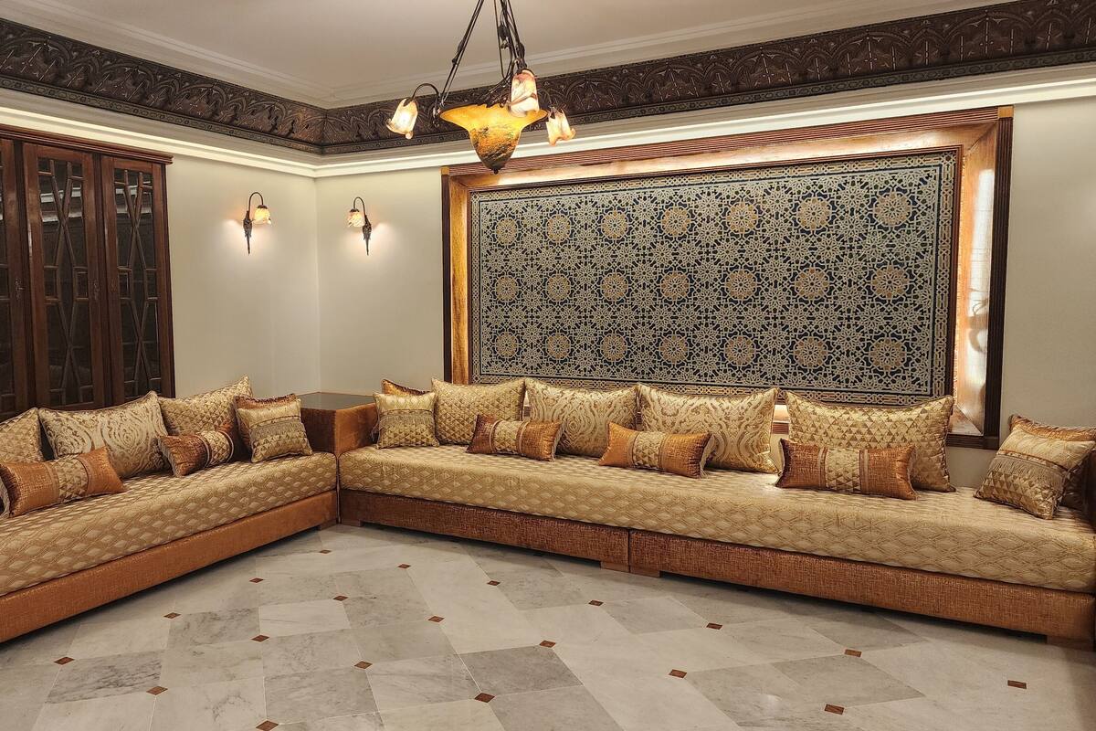 Um sofá de canto com almofadas estampadas, um painel decorativo na parede e um candelabro.
