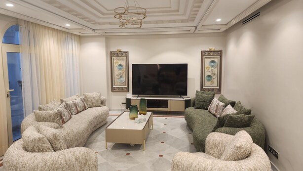 Een moderne woonkamer met een grote flatscreen televisie, twee banken, een salontafel en decoratieve wandkunst.