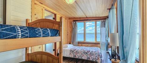 Una cabaña con literas, una cama individual, un escritorio con lámpara y una ventana con cortinas.