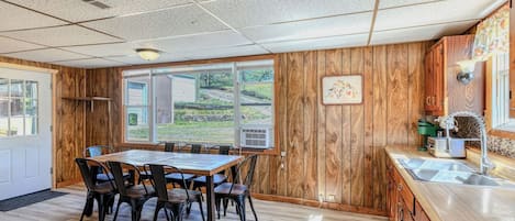 Una cocina con paneles de madera, una mesa de comedor con sillas, un ventanal con vistas a la vegetación y un lavamanos con accesorios modernos.