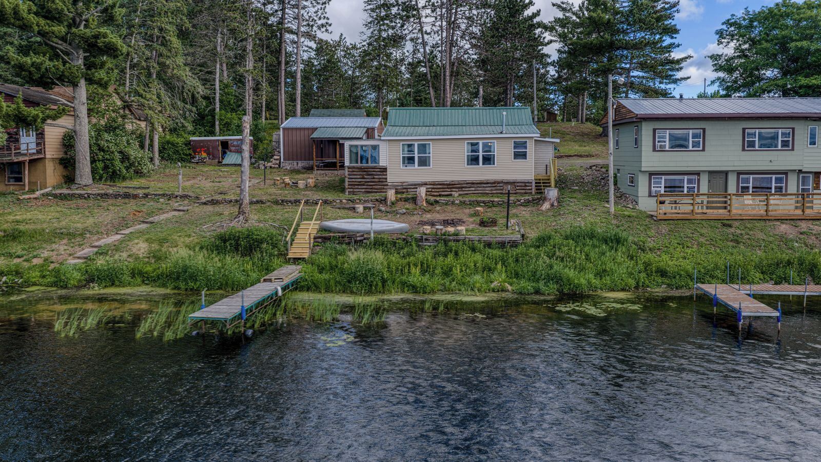 A lakeside cabin with a dock, surrounded by trees and a small building.