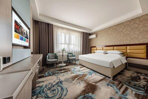 A hotel room with a bed, a desk, a chair, a small table, and a TV. - Qiyu Hotel (Burqin)
