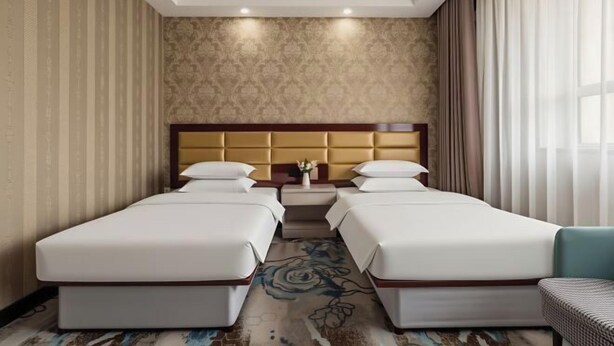 A hotel room with two beds, a headboard, a small table, and a window with curtains.