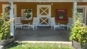 A building with a red roof, white exterior walls, and a porch with white rocking chairs and potted plants.