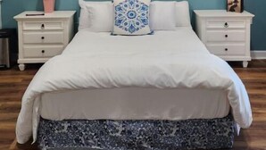 A bedroom with a bed, two nightstands, a painting of flowers, and a blue wall.