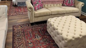 A bedroom with a bed, a beige sofa, a tufted ottoman, a nightstand, and a lamp.