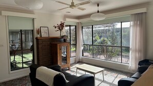 A living room with a fireplace, a sofa, a coffee table, and large windows offering a view of the outdoors. - Close to the Shops Beach, Perfect for 2 Families (Inverloch)