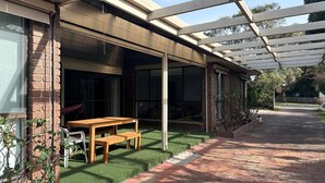 A covered patio with a wooden table and bench, a brick wall, and a view of the backyard. - Close to the Shops Beach, Perfect for 2 Families (Inverloch)