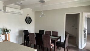 A dining area with a table and chairs, an air conditioning unit, a wall-mounted shelf with plants, and a chandelier. - Close to the Shops Beach, Perfect for 2 Families (Inverloch)