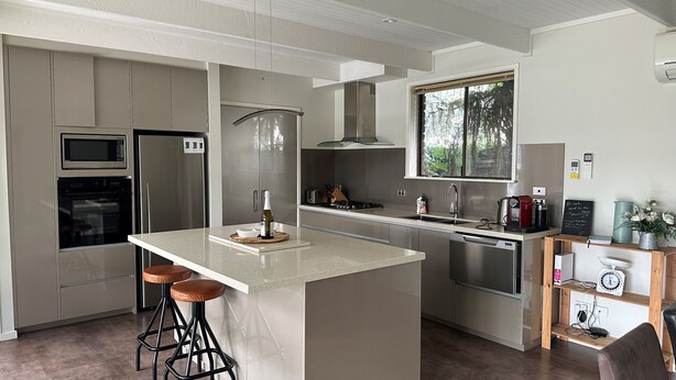 A modern kitchen with a central island, stainless steel appliances, and a window overlooking greenery. - Close to the Shops Beach, Perfect for 2 Families (Inverloch)