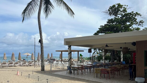 Een restaurant aan het strand met terras, palmbomen en uitzicht op de oceaan.