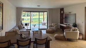 Een ruime woonkamer met een eetgedeelte, een televisie en uitzicht op een golfbaan.