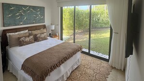 Een slaapkamer met een groot bed, een schilderij van vogels, een televisie en uitzicht op een tuin door een schuifdeur.