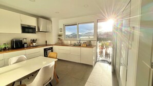 A modern kitchen with white cabinetry, a dining area with a table and chairs, and a view through a glass door to an outdoor balcony. - Spacious serene 4-bedroom house, central location with garden, terraces, fitness (Funchal)