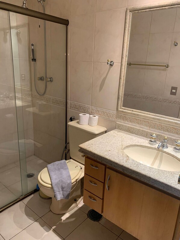 A bathroom with a glass-enclosed shower, a toilet, a sink with a vanity, and a mirror. - Get a Flat 909 Bienal-Ibirapuera (São Paulo)